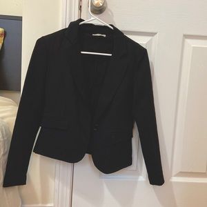 Short black suit jacket, low one-button closure, fake front pockets